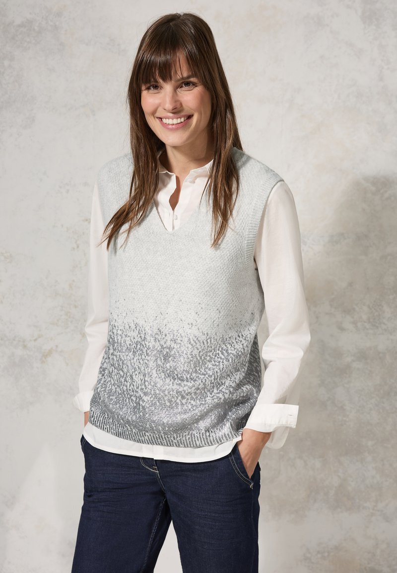 Chaleco de punto gris claro con escote en V y patrón texturizado, que presenta un efecto ombré que transiciona al plateado. Llevado sobre una camisa blanca con cuello.