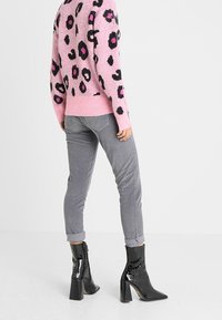 Maglione rosa con macchie di leopardo nere e fucsia, abbinato a pantaloni slim fit grigi e stivaletti neri lucidi con tacco a blocco.