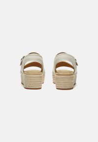 Sandali bianchi in pelle con retro aperto, caratterizzati da una zeppa in stile espadrille intrecciata e un accento decorativo a forma di fibbia.