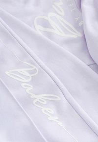 Lys lilla stof med hvid, blank tekst, der staver "Bager" med et buet linjemotiv, med en glat, blød tekstur.