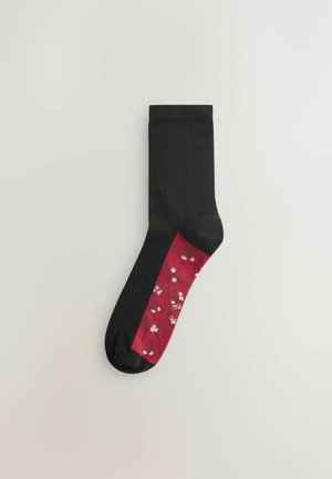 Svart socka med en röd blommönstrad sektion som har små vita blommor. Slät textur och standard längd.