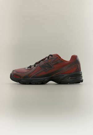 Chaussure de sport New Balance rouge et noire avec mesh et matériaux synthétiques, semelle noire et lacets noirs, vue de côté sur un fond uni.