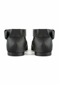 Pantofi din piele neagră cu toc mic și curele la gleznă. Textură netedă, design minim. Au un vârf rotunjit și accente din metal.