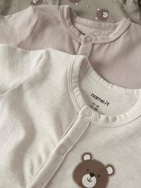 Tre babybodys i mjuk bomull, med en gräddfärgad body med björntryck, en ljusrosa body och en mönstrad grå med björnar.
