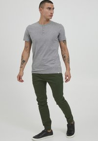 Gray short-sleeve henley shirt with button detailing, paired with fitted green jogger pants and black sneakers. Casual design, stretchy fabric.
