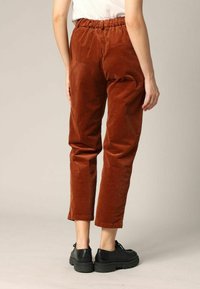 Pantalons en velours côtelé marron avec une taille élastique, longueur cropped et une poche arrière. La texture est nervurée, avec une finition douce.