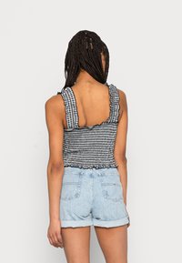 Top cropped em gingham preto e branco com alças franzidas, textura pregueada e bainha com um acabamento em ondulação, combinado com calções de ganga claros.