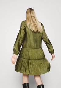 Grön satin klänning med långa ärmar, featuring en lager-på-lager kjol och flödande textur, som framhäver en glänsande finish och subtil lyster.