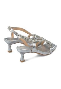 Silverfärgade sandaler med remmar och kvadratisk tå, dekorerade med rhinestones, med en låg, utfläkt klack och en slät metallisk yta.