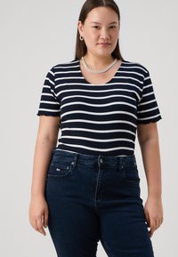 Marineblå og hvite stripete kortermet skjorte med rund hals, ribbet tekstur og bølgete kant, kombinert med mørke denimjeans.