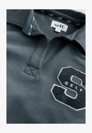 Siva polo majica s teksturiranim, izvezenim "S" logotipom i "SELF" u bijeloj boji, s klasičnim ovratnikom i detaljem trokutastog šivanja.