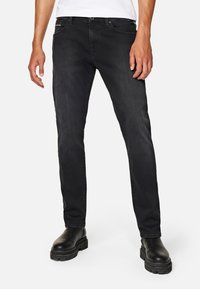 Vaqueros de denim negro con un corte ajustado, que presentan un diseño tradicional de cinco bolsillos y una textura sutilmente desvanecida. Combinados con botas gruesas negras.