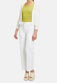 Bílý žebrovaný cardigan přes zelený top na ramínka, doplněný o bílé široké džíny a béžové platformové sandály s otevřenou špičkou. Minimum doplňků.