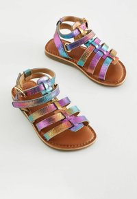 Sandaler med remmar och en brun läderinnersula samt iriserande metallremmar i blått, lila och guld. Spänne vid vristen.