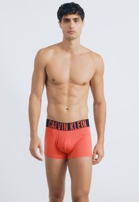 Crvene bokserice sa crnim Calvin Klein pojasom, sa uskim fitom i glatkom teksturom. Dizajn naglašava udobnost i jednostavan stil.