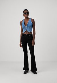 Denim kratki prsluk s dubokim V-izrezom, detaljima na dugmadima i crnim širokim trapericama, upotpunjen tamnim sunčanim naočalama i elegantnim crnim cipelama.