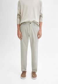 Lichtgrijze broeken van zacht stof, met een rechte pasvorm, knoopsluiting en zijzakken, gecombineerd met een lichtbeige overhemd met lange mouwen.