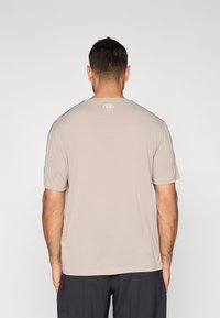 Beige atletisk t-skjorte med korte ermer, rund hals og subtil logo på baksiden. Jevn tekstur, tettsittende design, ensfarget stoff.