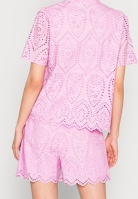 Set composto da top a maniche corte e pantaloni corti rosa, caratterizzato da dettagli a taglio e bordi ondulati, realizzato in tessuto leggero con finitura texture.