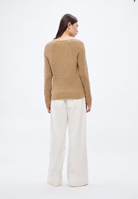 Beige strikkegenser med vid hals og ribbet tekstur, kombinert med løstsittende hvite bukser med oppbrettede kanter.