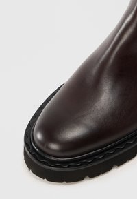 Botte cheville en cuir marron avec une finition lisse, bout rond et une semelle en caoutchouc noir texturé à bord festonné.