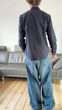 Sort langærmet skjorte med rundet kant og manchetter med knapper, kombineret med blå vide denimjeans med lommepatches.
