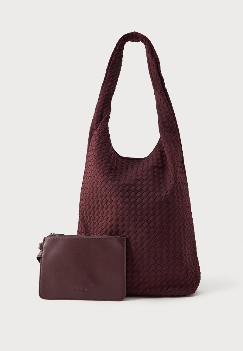 Sac à épaule tissé bordeaux foncé avec pochette zippée lisse assortie placée devant sur un fond clair.