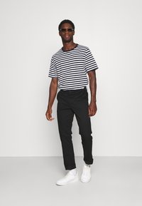 Tricou cu mânecă scurtă, în dungi alb-negru, purtat cu pantaloni negri conici și teniși albi. Accesoriile includ ochelari de soare închiși la culoare.
