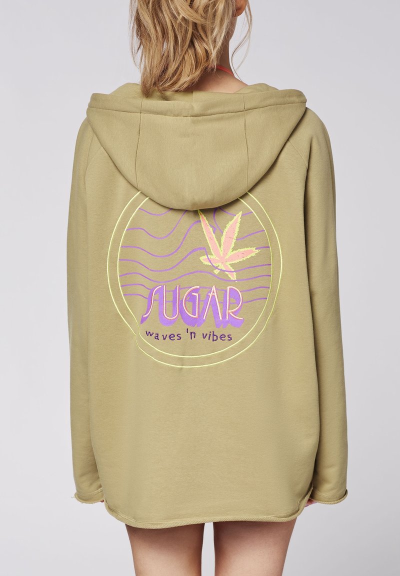 Sweat à capuche vert olive, tissu doux, avec un grand motif circulaire à l'arrière portant l'inscription « SUGAR » en violet et un dessin de feuille, ainsi que des vagues.