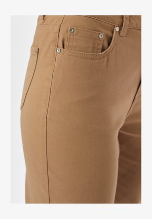 Zbliżenie na brązowe spodnie, ukazujące przednie i kieszeń na monety z metalowymi nitami oraz szczegółowym przeszyciem na materiale.