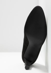 Chaussure en daim noir avec un bout pointu et un design élégant. La semelle est plate avec un léger nervurage et affiche la taille 37 au-dessous.