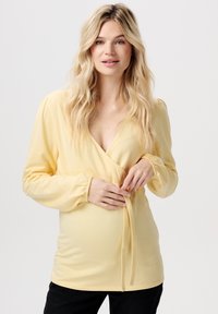 Geel wikkelblouse met lange mouwen, diepe V-hals, elastische manchetten en een strikdetail op de taille. Zacht, glad stof met een getailleerde pasvorm.