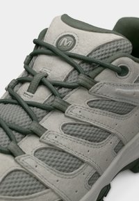 Ανοιχτό γκρι παπούτσι πεζοπορίας με υφή στην επάνω επιφάνεια, πράσινες λεπτομέρειες, τμήματα από δίχτυ και ενισχυμένη μύτη. Διαθέτει χοντρές κορδόνια και επενδυμένο γιακά.