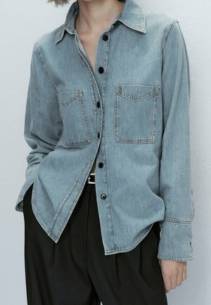 Vaaleansininen farkkupaita kauluskauluksella, nappikiinnityksellä, kahdella rintataskulla ja pitkillä hihoilla, jossa rento istuvuus ja rispaantuneet reunat.