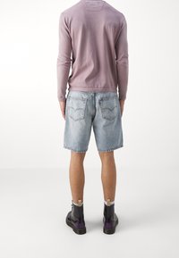 Long-sleeve lavender shirt, light blue denim shorts with frayed edges, and black ankle boots with purple accents, viewed from the back.