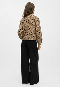 Blusa beige con estampado floral negro y mangas abullonadas, combinada con pantalones de pierna ancha negros de cintura alta. Textura de tela suave.