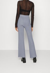 Höghöga, ljusblå ribbade stickade byxor med utsvängd ben, i kombination med en genomskinlig svart långärmad topp och kraftiga svarta klackstövlar.