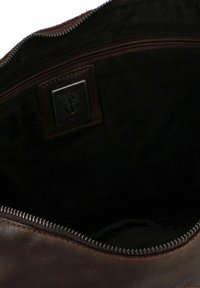 Interno di una borsa in pelle marrone scuro con rivestimento in tessuto nero, una tasca con zip e un piccolo pezzo quadrato con un simbolo di ancora.