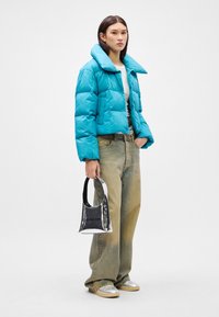 Skraćena tirkizna puffer jakna s velikim kragnom, uparena s labavim izbljeđenim trapericama i sjajnom srebrnom torbom. Ravne srebrne cipele.