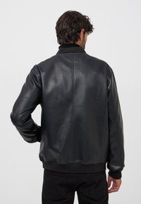 Czarna skórzana kurtka bomberka z prążkowanym kołnierzem i mankietami. Gładka tekstura, dopasowany krój i prosta detal na tylnym szwie.