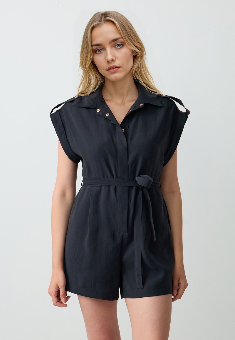 Zwarte, mouwloze romper met een kraag, knopen aan de voorkant en een strikriem in de taille. Bevat gouden accenten en een comfortabele pasvorm.