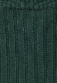 Dunkelgrüner Strickstoff mit vertikalen Rippenmustern. Die Textur ist weich mit einem leichten Stretch und wirkt gemütlich.