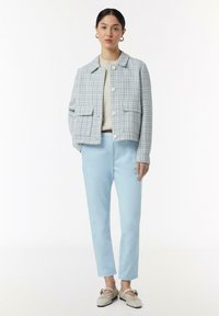 Lichtblauw geweven blazer met twee voorkepten, gecombineerd met lichtblauwe broek en gestreepte schoenen. Neutrale trui onder de blazer.