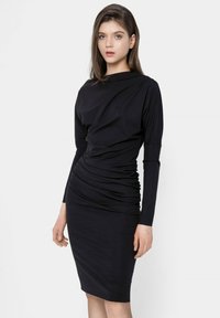 Czarna sukienka z długim rękawem wykonana z miękkiego materiału; ma zwisające wykończenie i dopasowany fason, kończący się tuż nad kolanem.