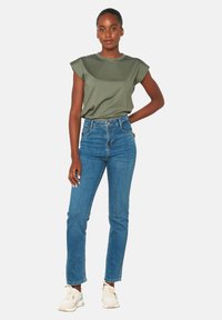 Alyvų žalios spalvos trumpomis rankovėmis palaidinė, aukštu liemeniu mėlynos džinsai ir šviesūs sportiniai bateliai. Lygus audinys, pritaikyta fasonas ir klasikinio tiesaus kirpimo dizainas.