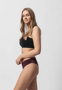 Bralette nera e mutandine bordeaux con pizzo. L'intimo presenta una texture morbida con bordi scallop e un design aderente.
