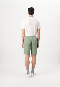 Shorts en coton verts avec une taille élastique et une poche arrière, associés à un t-shirt blanc, des chaussettes grises et des baskets blanches.