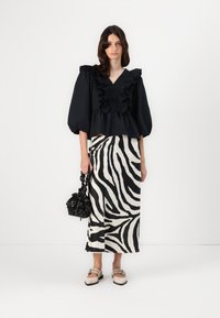 Svart bluse med volanger og knappedetaljer, parret med et zebrastripe skjørt i svart og krem, og en svart veske med blomsterakses.