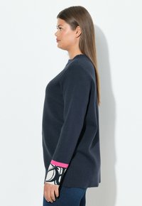 Marineblauer Langarm-Pullover mit lockerer Passform, ausgestattet mit gemusterten Bündchen in Weiß und rosa Akzenten. Weicher, struktureller Stoff, lässiges Design.