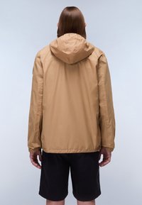 Letvægts, hættetrøje i tan farve, lavet af glat, vandafvisende materiale, med elastiske manchetter og en afslappet pasform, parret med mørke shorts.